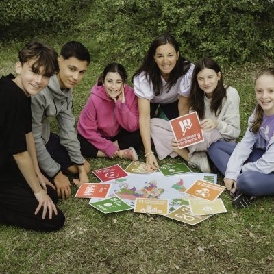 A group of students with a teacher, sitting on the grass and smiling.