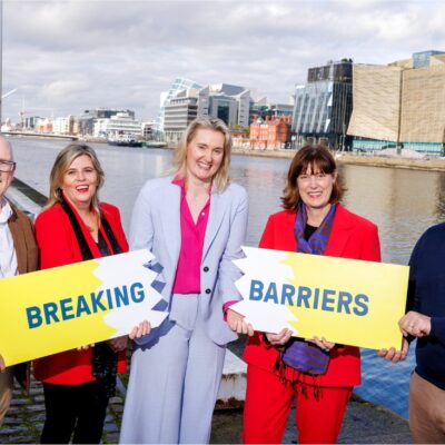 A group of five people smiling and holding a sign that says Breaking Barriers. The sign is broken in two.