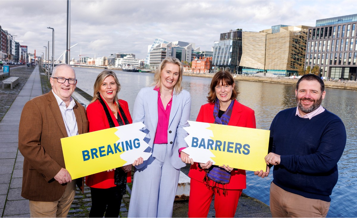 A group of five people smiling and holding a sign that says Breaking Barriers. The sign is broken in two.