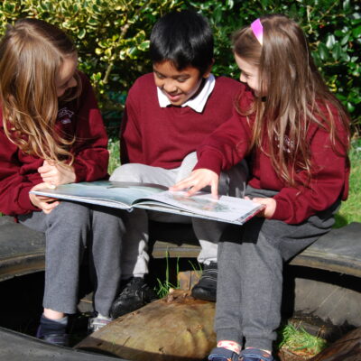 Three school children huddled around a book reading outdoors