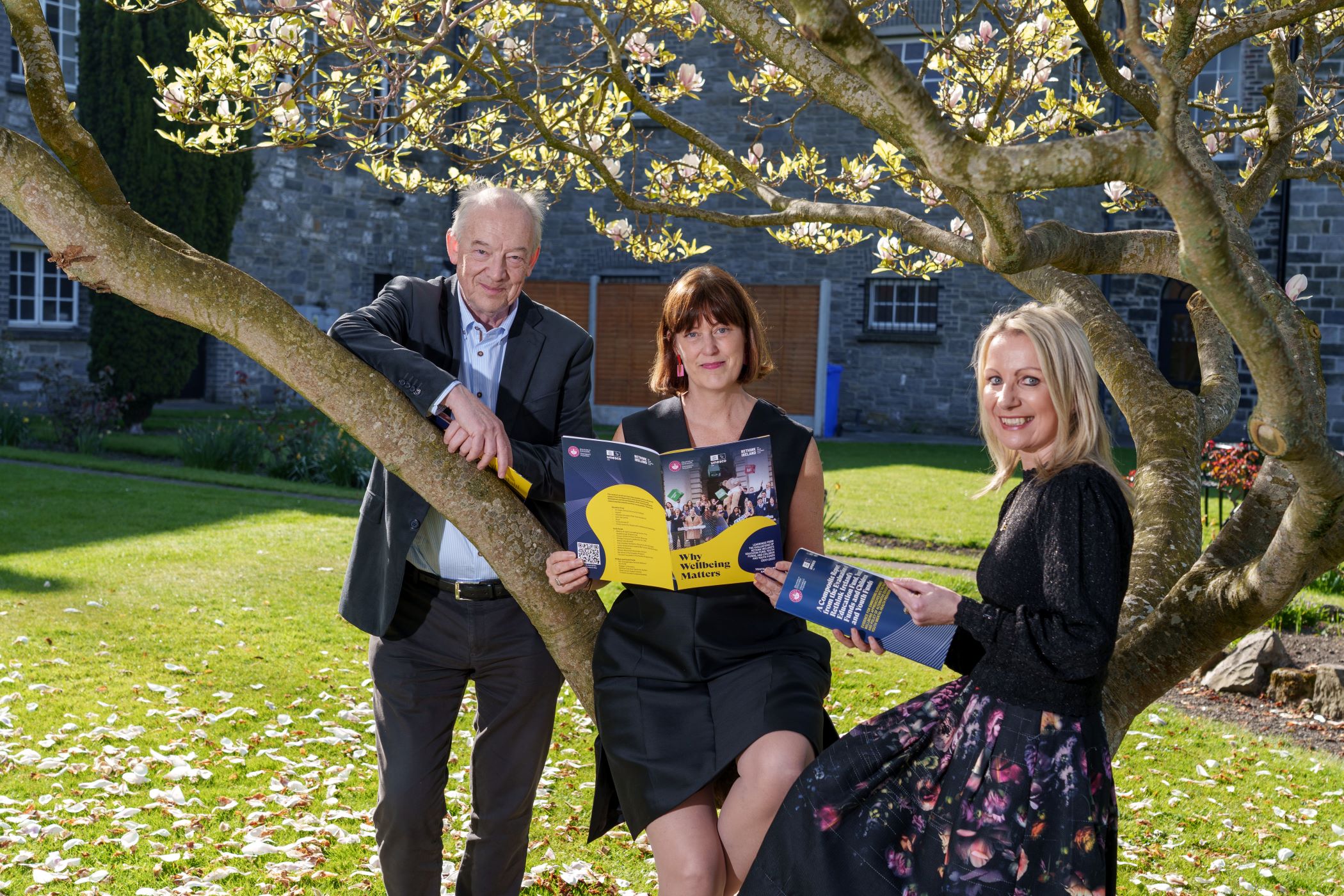 Man and two women sit around and on tree branch holding academic reports