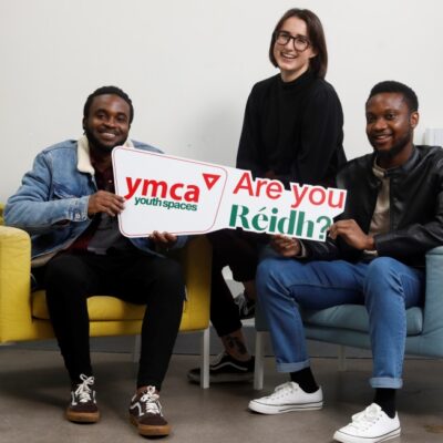 Three smiling people holding a sign that reads YMCA, Are you Réidh?