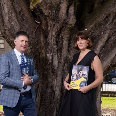 Man and woman hold copy of report in front of tree on a sunny day