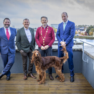 Four men smiling on balcony including Limerick Mayor with Irish red setter in foreground