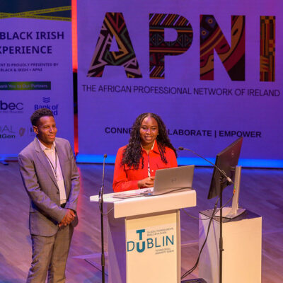 A man and woman smiling in front of a lectern at a conference