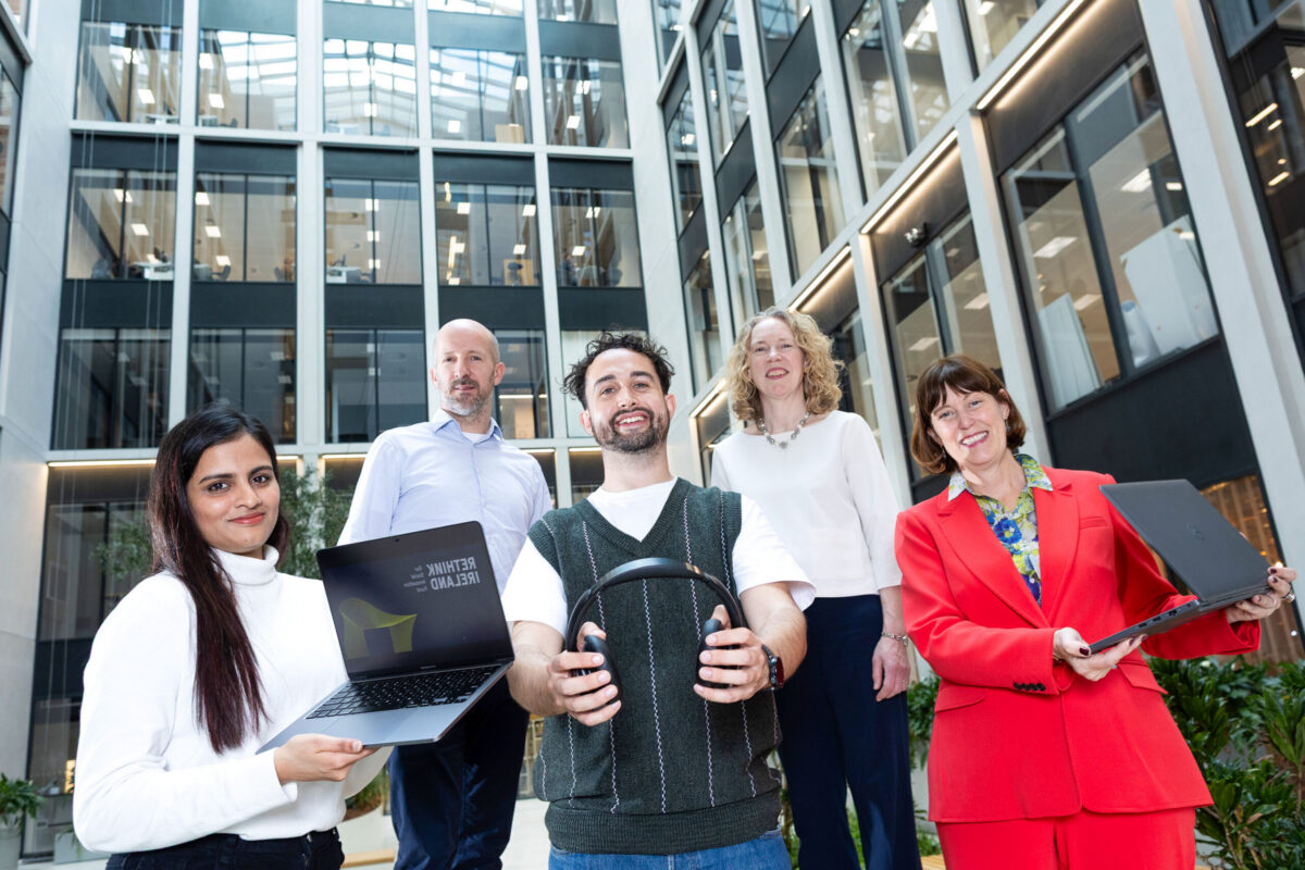 5 people smiling in a room and 3 holding tech devices