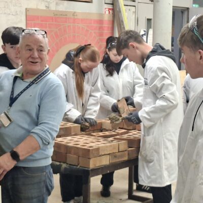 Adult showing young people how to lay bricks