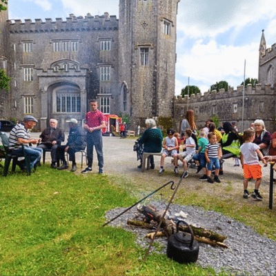 Group of people of all ages standing and sitting outside a castle chatting and playing