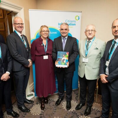 group of 5 men and 1 women standing in front of a poster with one person holding a brochure