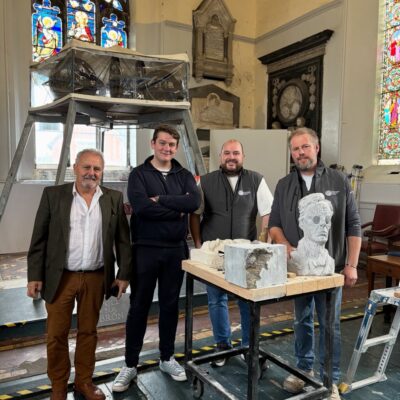 Four men standing at a table with a stone model of a bust